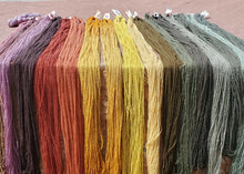 Set of colorful yarn skeins hanging against a stone wall.